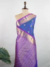 Kanchipuram Silk In a striking combination of blue and purple, this Vairavoosi Kanchipuram saree in 100% pure silk is woven with pure zari and finished with a medium border. Bold yet elegant, this drape mirrors the rhythm of traditional craft. A regal weave for those who carry confidence in colour. #Manoranjitham #VairavoosiWeave #KanjivaramSilks #HandloomStory #BoldAndTraditional Sreemaata - Manoranjitham Weaves - Handloom Store