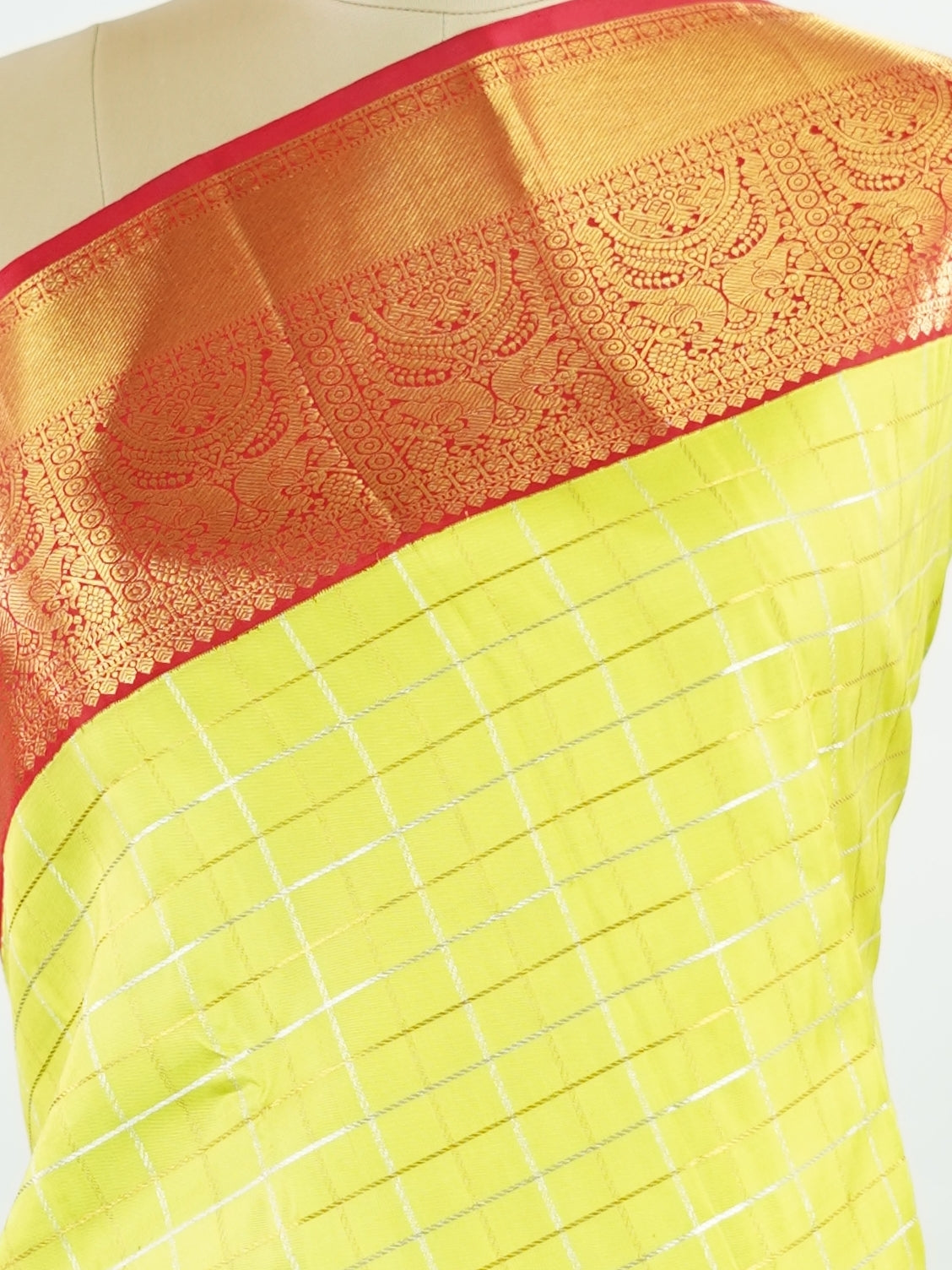 Kanchipuram Silk Beautiful traditional Kanjivaram saree featuring a vibrant Leaf Green body adorned with exquisite gold and silver checks, creating a rich and radiant appearance. The striking Red border is embellished with majestic Annapakshi motifs, adding a touch of heritage and timeless elegance. An intricately woven pallu with classic diamond motifs enhances the grandeur and sophistication of the drape. Paired with a plain Red blouse, this masterpiece is perfect for weddings, festive occasions, and trad