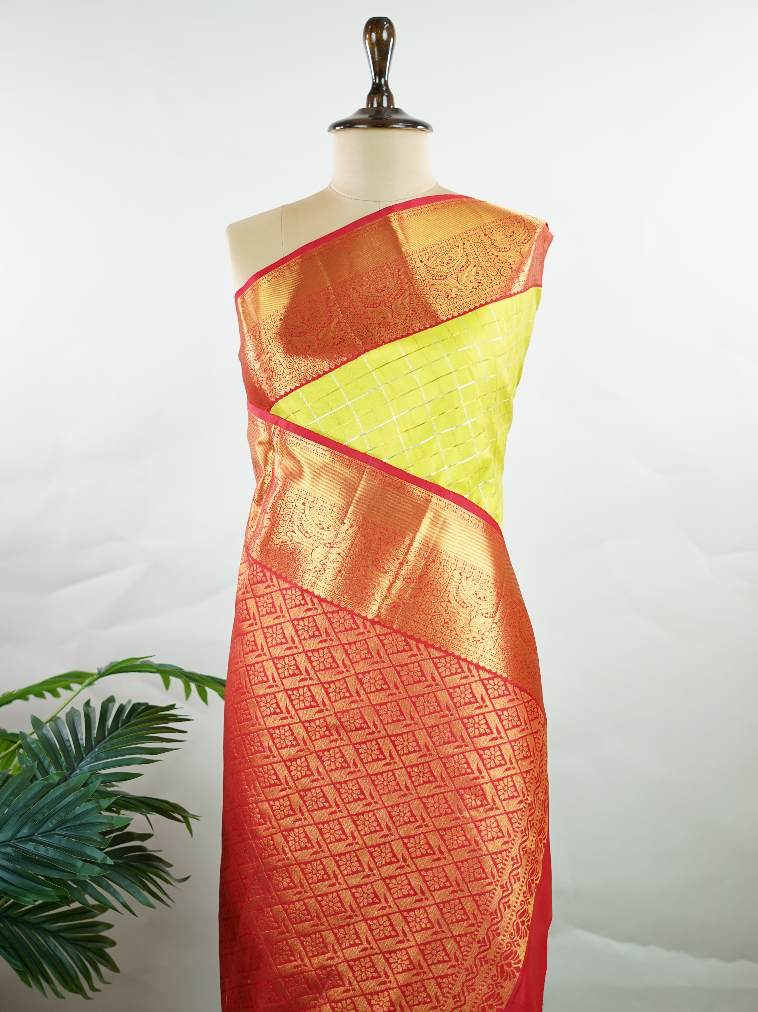 Kanchipuram Silk Beautiful traditional Kanjivaram saree featuring a vibrant Leaf Green body adorned with exquisite gold and silver checks, creating a rich and radiant appearance. The striking Red border is embellished with majestic Annapakshi motifs, adding a touch of heritage and timeless elegance. An intricately woven pallu with classic diamond motifs enhances the grandeur and sophistication of the drape. Paired with a plain Red blouse, this masterpiece is perfect for weddings, festive occasions, and trad