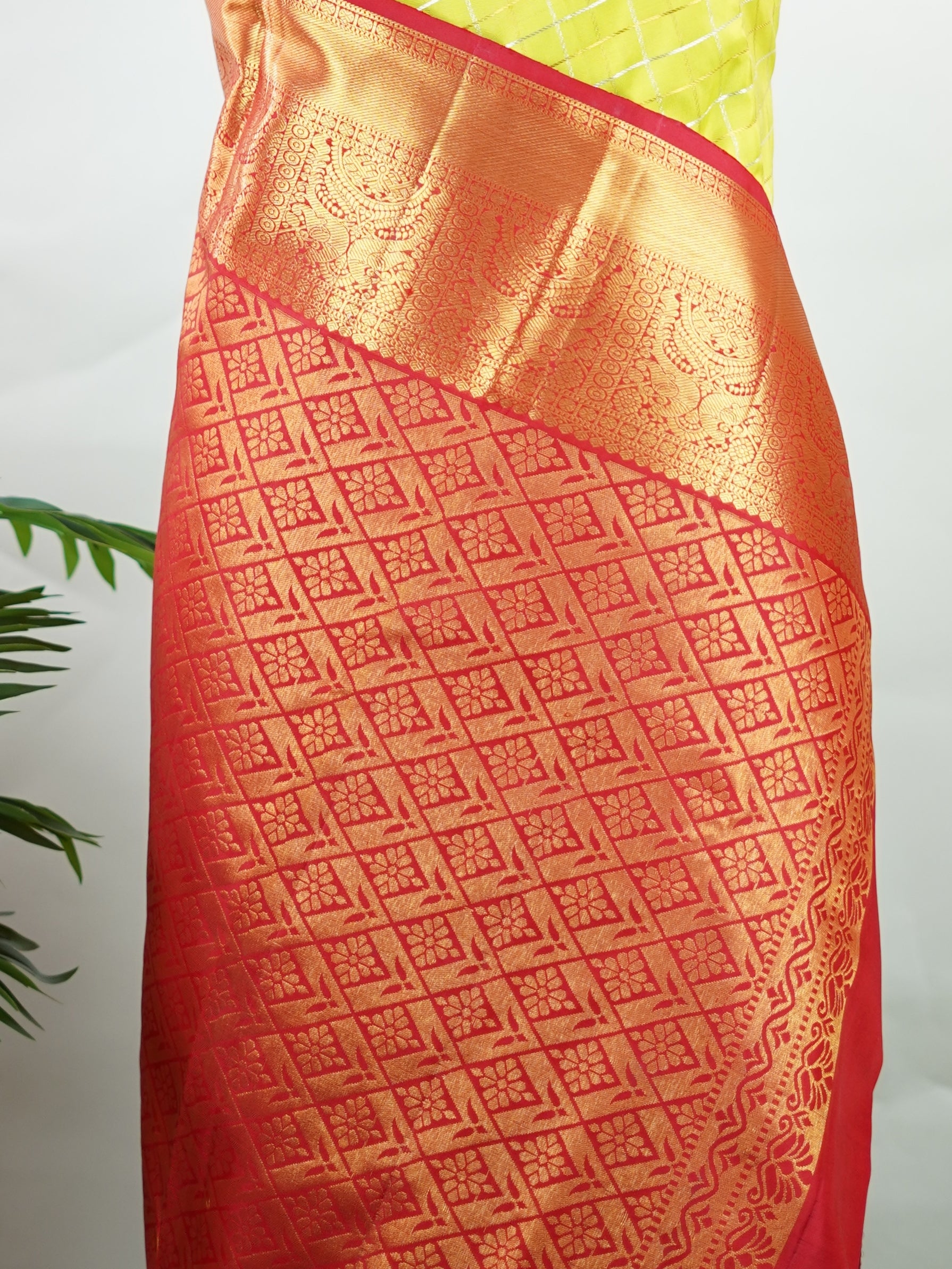 Kanchipuram Silk Beautiful traditional Kanjivaram saree featuring a vibrant Leaf Green body adorned with exquisite gold and silver checks, creating a rich and radiant appearance. The striking Red border is embellished with majestic Annapakshi motifs, adding a touch of heritage and timeless elegance. An intricately woven pallu with classic diamond motifs enhances the grandeur and sophistication of the drape. Paired with a plain Red blouse, this masterpiece is perfect for weddings, festive occasions, and trad