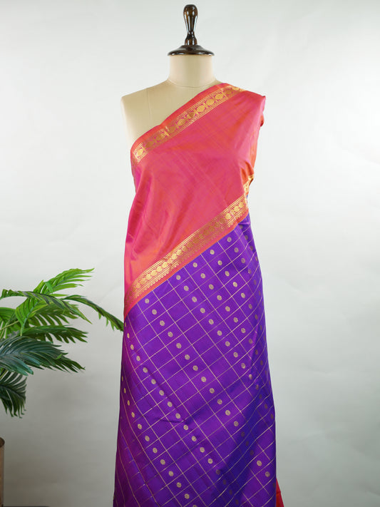 Kanchipuram Silk Elegant and striking, this violet Kanjivaram saree is woven in luxurious 100% pure silk for a rich, graceful drape. The body is adorned with delicate buttis, while the contrasting pinkish orange gap border adds a bold and contemporary touch. A perfect fusion of classic tradition and statement design—ideal for weddings and festive celebrations Mahamaya - Manoranjitham Weaves - Handloom Store