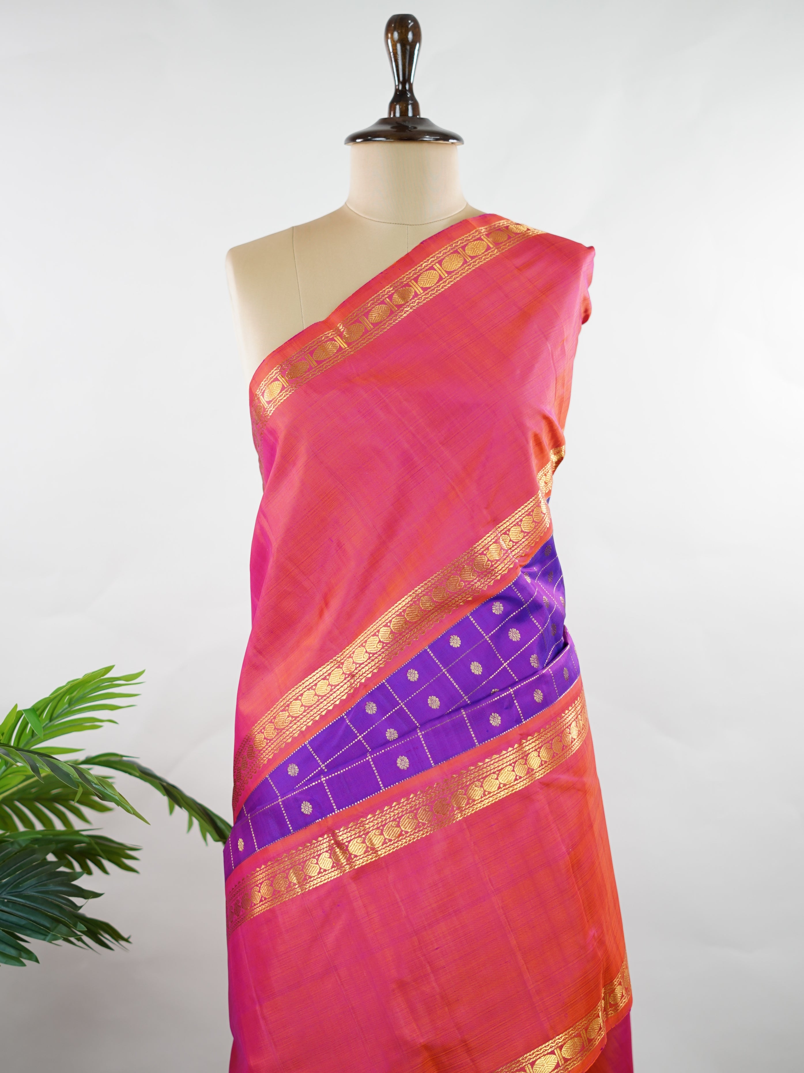 Kanchipuram Silk Elegant and striking, this violet Kanjivaram saree is woven in luxurious 100% pure silk for a rich, graceful drape. The body is adorned with delicate buttis, while the contrasting pinkish orange gap border adds a bold and contemporary touch. A perfect fusion of classic tradition and statement design—ideal for weddings and festive celebrations Mahamaya - Violet Pure Kanjivaram Silk Saree - Manoranjitham Weaves - Handloom Store