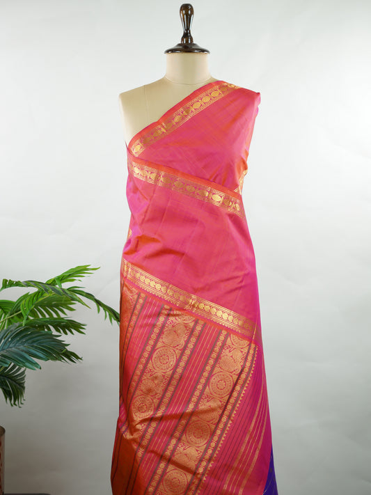 Kanchipuram Silk Elegant and striking, this violet Kanjivaram saree is woven in luxurious 100% pure silk for a rich, graceful drape. The body is adorned with delicate buttis, while the contrasting pinkish orange gap border adds a bold and contemporary touch. A perfect fusion of classic tradition and statement design—ideal for weddings and festive celebrations Mahamaya - Manoranjitham Weaves - Handloom Store
