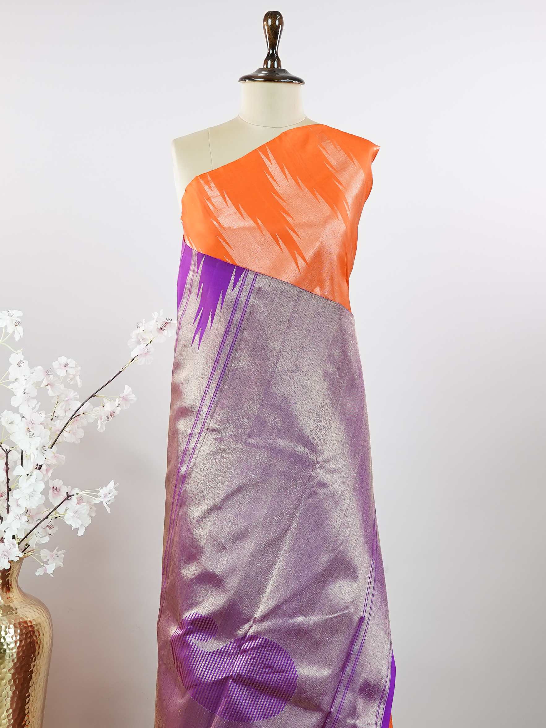 Kanchipuram Silk Striking and festive, this orange Kanjivaram saree is enhanced with rich purple contrast and detailed 8-kol borders. The luxurious silk drape and vibrant colour pairing make it an ideal choice for weddings and grand celebrations. Keertana - Orange Pure Kanjivaram Silk Saree - Manoranjitham Weaves - Handloom Store