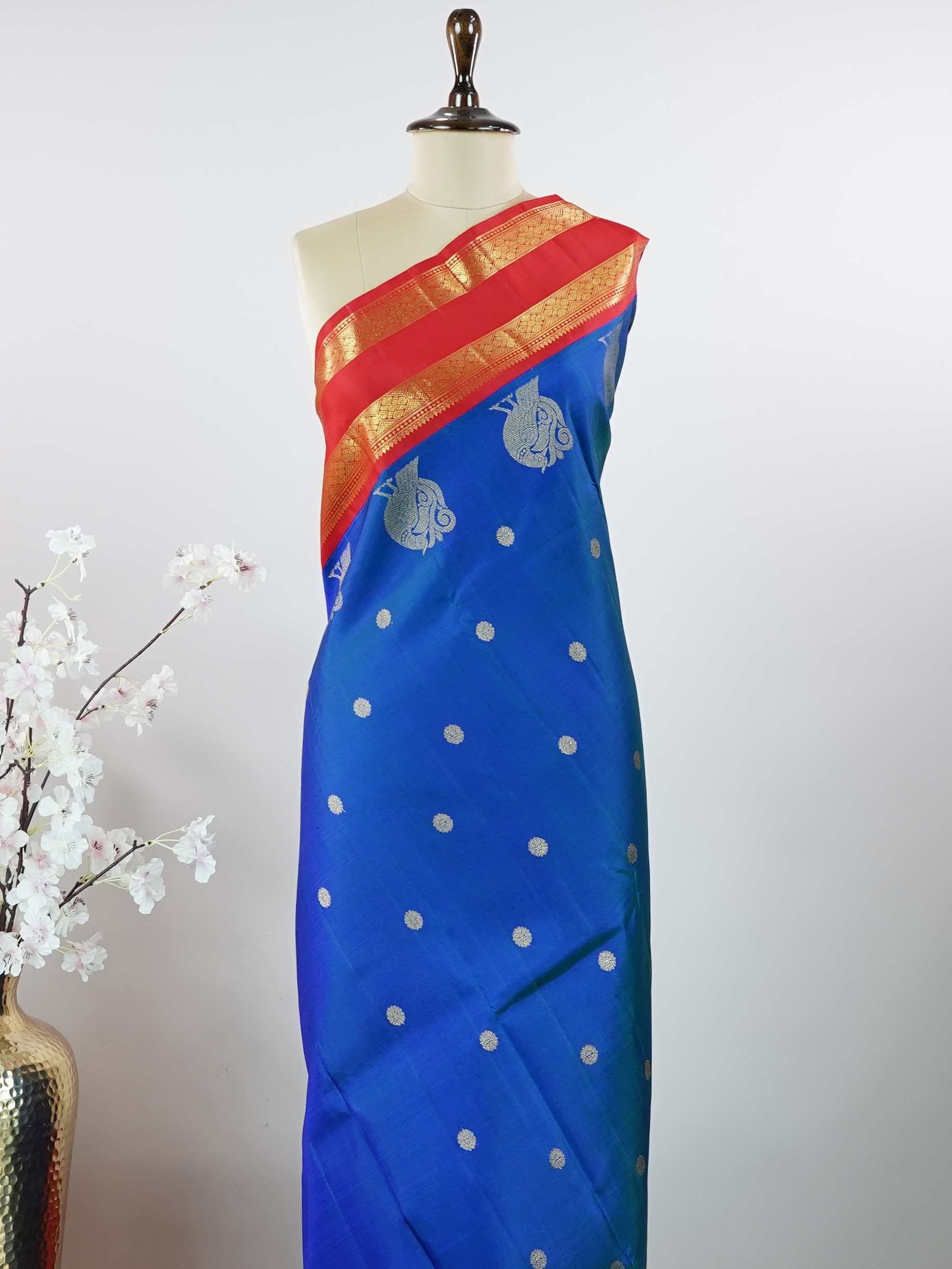 Kanchipuram Silk This exquisite Kanjivaram saree features a blue body with a striking red border, crafted from 100% pure silk.br
The body showcases a Korvai/Kuttu pattern, adorned with delicate flower motifs and peacocks flanking the border.br
Finished with elegant detailing, it beautifully highlights traditional handloom craftsmanship and timeless Kanchipuram artistry. Shivashakti - Blue Pure Kanjivaram Silk Saree - Manoranjitham Weaves - Handloom Store