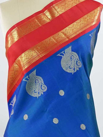 Kanchipuram Silk This exquisite Kanjivaram saree features a blue body with a striking red border, crafted from 100% pure silk.br
The body showcases a Korvai/Kuttu pattern, adorned with delicate flower motifs and peacocks flanking the border.br
Finished with elegant detailing, it beautifully highlights traditional handloom craftsmanship and timeless Kanchipuram artistry. Shivashakti - Blue Pure Kanjivaram Silk Saree - Manoranjitham Weaves - Handloom Store