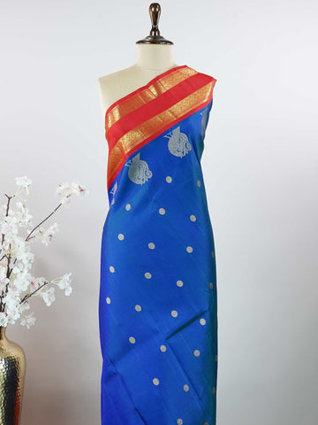 Kanchipuram Silk This exquisite Kanjivaram saree features a blue body with a striking red border, crafted from 100% pure silk.br
The body showcases a Korvai/Kuttu pattern, adorned with delicate flower motifs and peacocks flanking the border.br
Finished with elegant detailing, it beautifully highlights traditional handloom craftsmanship and timeless Kanchipuram artistry. Shivashakti - Blue Pure Kanjivaram Silk Saree - Manoranjitham Weaves - Handloom Store