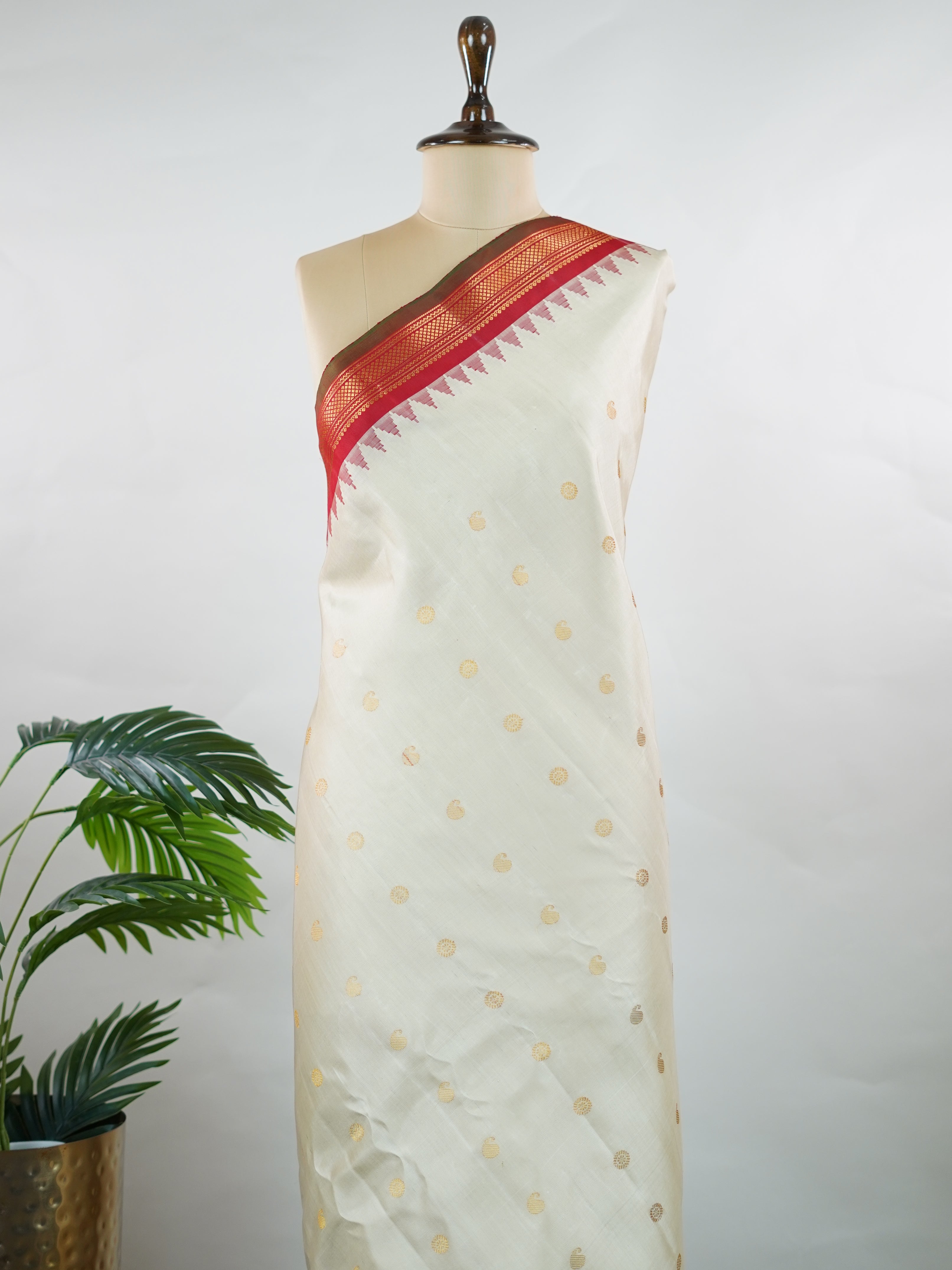 Gadwal Silk This elegant Gadwal saree features a beige body paired with a red border, crafted from 100% pure silk.br
The body is adorned with delicate gold mango and rudraksha buttis, adding a touch of traditional charm.br
Finished with a subtle small border, it showcases the exquisite handloom artistry of Gadwal weaving. Mangala - Beige Handloom Gadwal Silk Saree | Pure Silk | Zari Border - Manoranjitham Weaves - Handloom Store