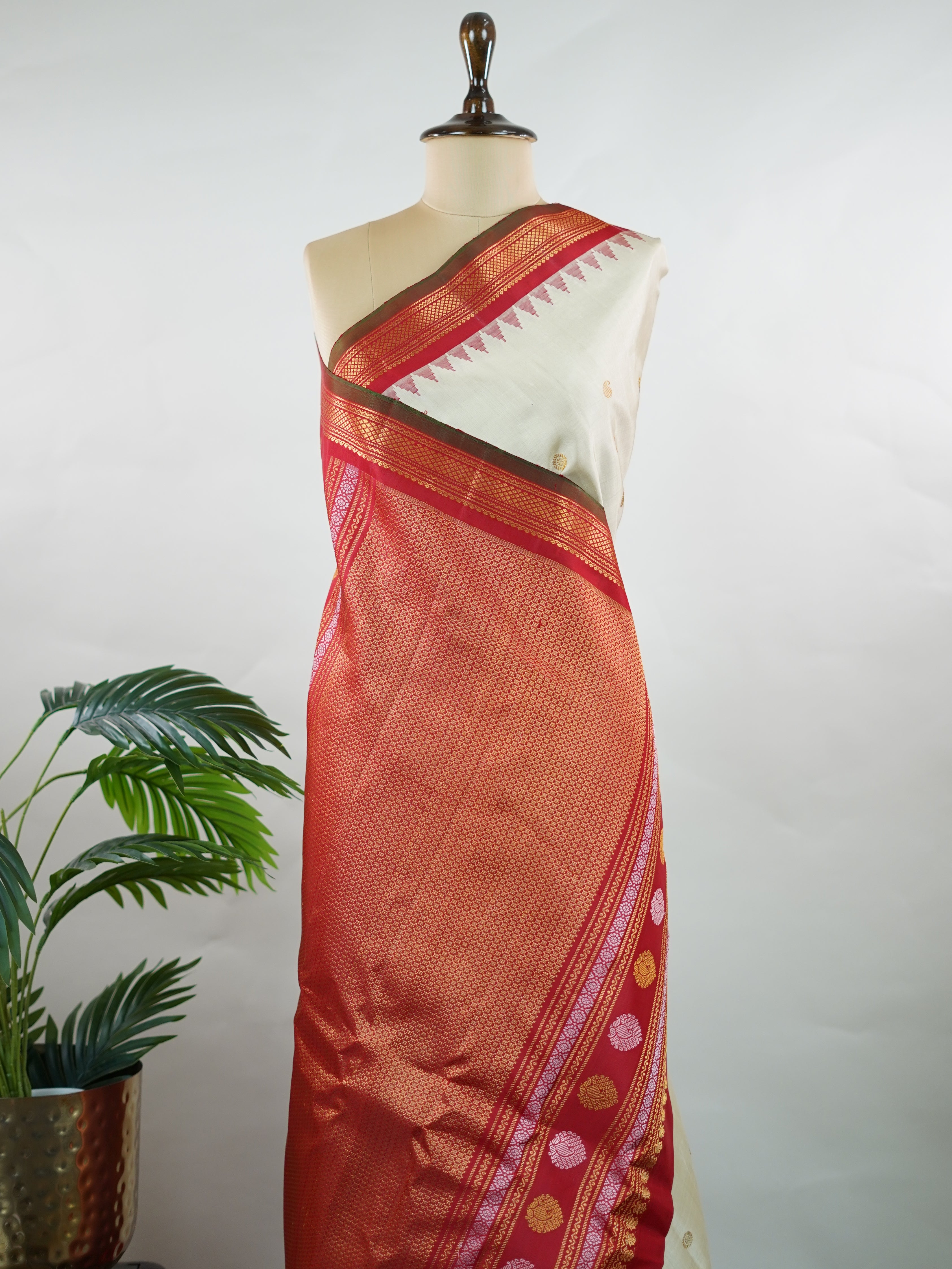 Gadwal Silk This elegant Gadwal saree features a beige body paired with a red border, crafted from 100% pure silk.br
The body is adorned with delicate gold mango and rudraksha buttis, adding a touch of traditional charm.br
Finished with a subtle small border, it showcases the exquisite handloom artistry of Gadwal weaving. Mangala - Beige Handloom Gadwal Silk Saree | Pure Silk | Zari Border - Manoranjitham Weaves - Handloom Store