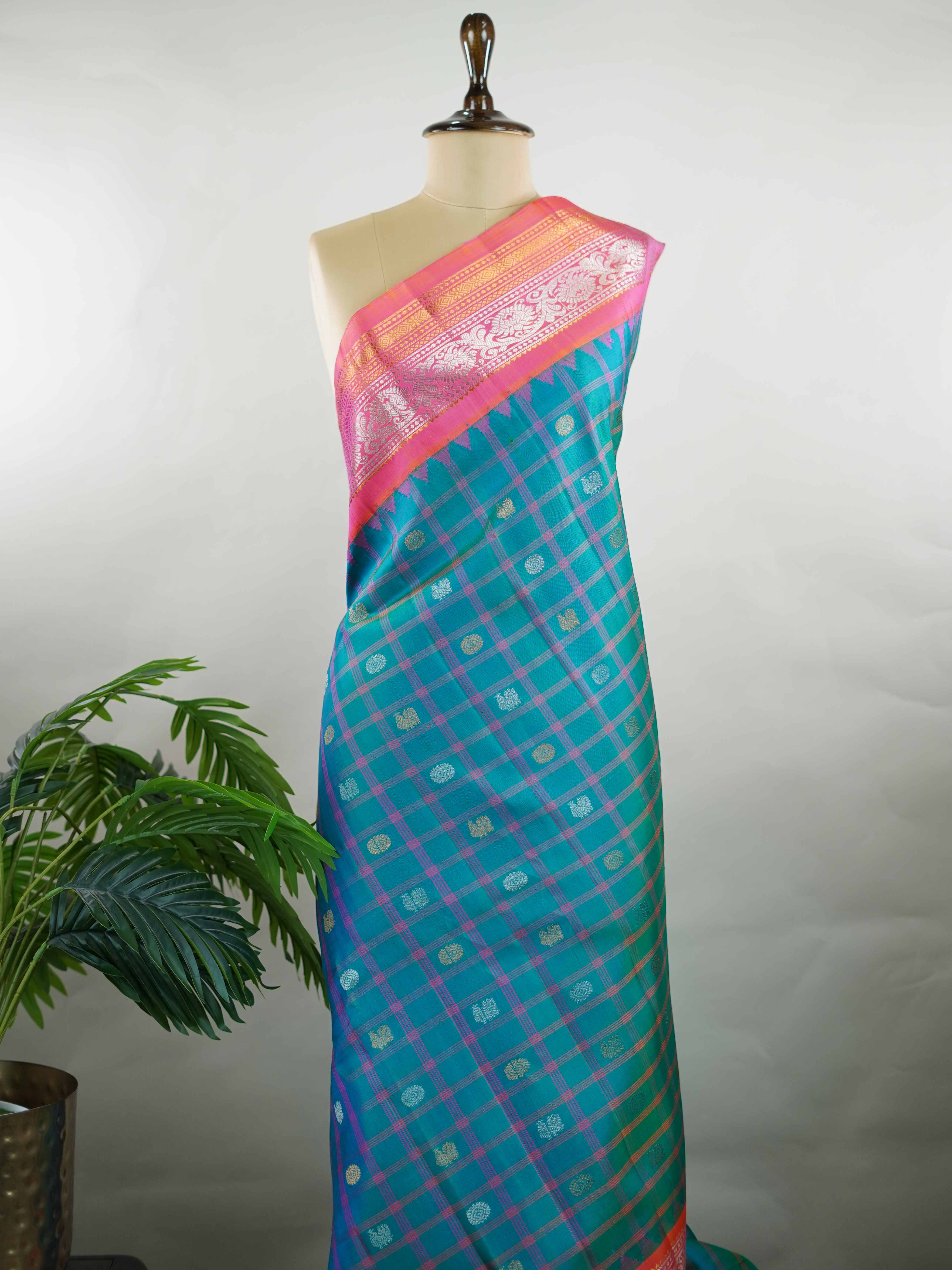 Gadwal Silk Stand out in elegance with this Gadwal saree in a rich peacock blue shade, paired beautifully with a contrasting pink blouse. The weave is adorned with silver and gold Chakram and Annapakshi buttas, showcasing exquisite traditional artistry. The fine detailing adds a regal charm, making it a perfect blend of heritage and sophistication.  Satyavati - Handloom Gadwal Silk Saree | Pure Silk | Zari Border - Manoranjitham Weaves - Handloom Store
