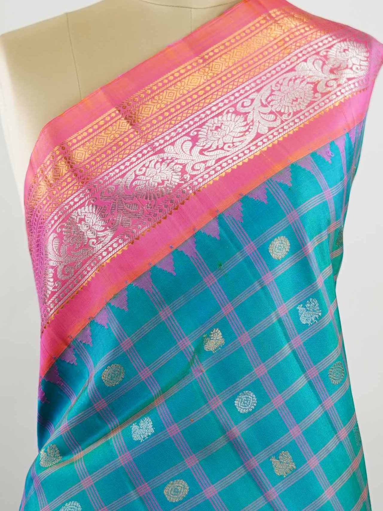 Gadwal Silk Stand out in elegance with this Gadwal saree in a rich peacock blue shade, paired beautifully with a contrasting pink blouse. The weave is adorned with silver and gold Chakram and Annapakshi buttas, showcasing exquisite traditional artistry. The fine detailing adds a regal charm, making it a perfect blend of heritage and sophistication.  Satyavati - Handloom Gadwal Silk Saree | Pure Silk | Zari Border - Manoranjitham Weaves - Handloom Store