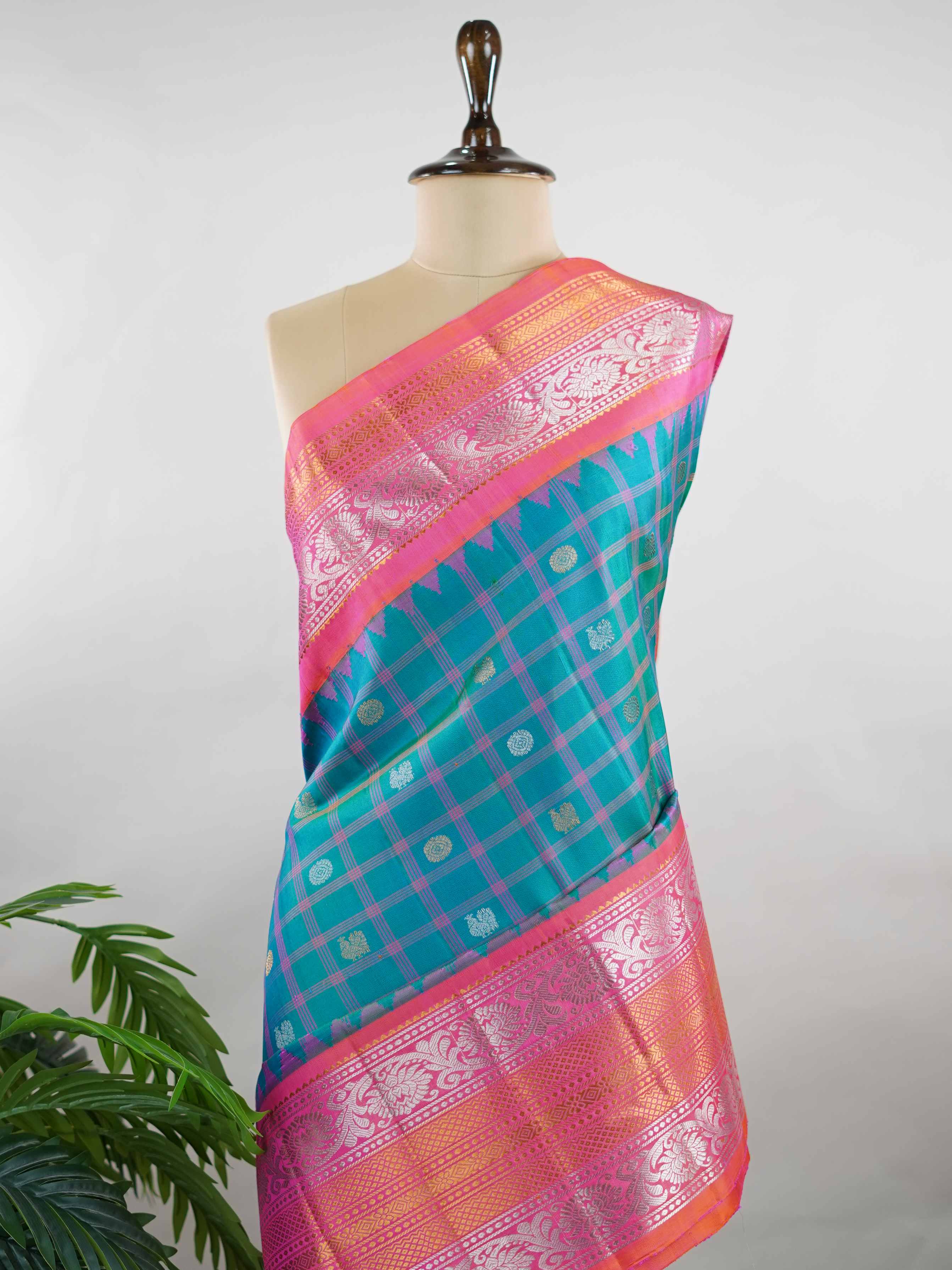 Gadwal Silk Stand out in elegance with this Gadwal saree in a rich peacock blue shade, paired beautifully with a contrasting pink blouse. The weave is adorned with silver and gold Chakram and Annapakshi buttas, showcasing exquisite traditional artistry. The fine detailing adds a regal charm, making it a perfect blend of heritage and sophistication.  Satyavati - Handloom Gadwal Silk Saree | Pure Silk | Zari Border - Manoranjitham Weaves - Handloom Store
