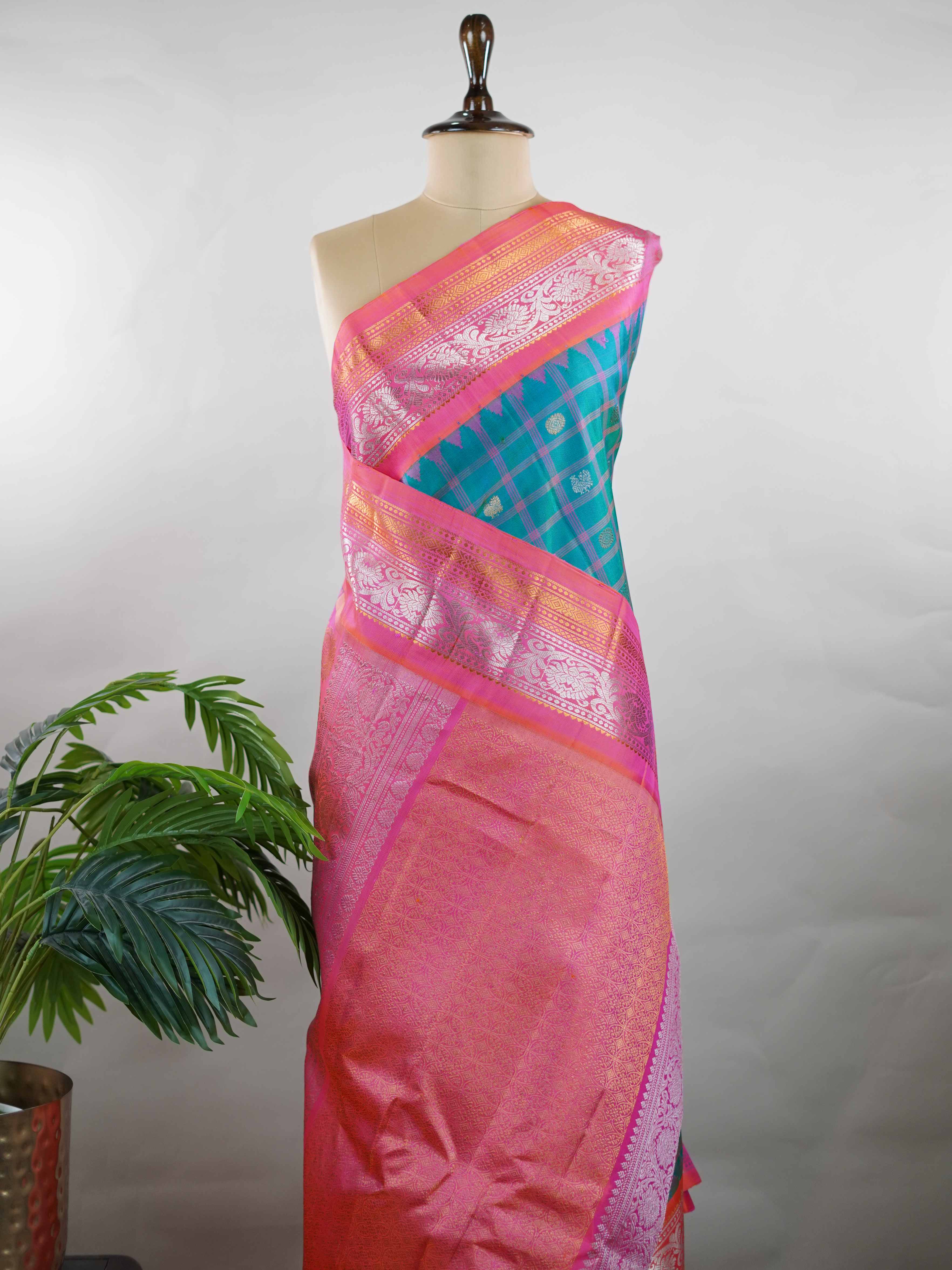 Gadwal Silk Stand out in elegance with this Gadwal saree in a rich peacock blue shade, paired beautifully with a contrasting pink blouse. The weave is adorned with silver and gold Chakram and Annapakshi buttas, showcasing exquisite traditional artistry. The fine detailing adds a regal charm, making it a perfect blend of heritage and sophistication.  Satyavati - Handloom Gadwal Silk Saree | Pure Silk | Zari Border - Manoranjitham Weaves - Handloom Store