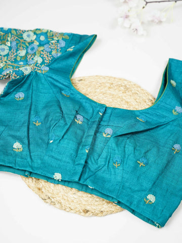 Tussar This elegant peacock blue Tussar designer blouse features finely stitched hand embroidery work. The front is adorned with small floral motifs, adding a delicate and graceful charm.br data-start=182 data-end=185The back is fully detailed with rich embroidery, showcasing intricate craftsmanship.br data-start=269 data-end=272Perfect for ethnic wear, it creates a bold, stylish, and beautifully balanced traditional look. Ira - Tussar Silk Saree | Hand Embroidered - Manoranjitham Weaves - Handloom Store