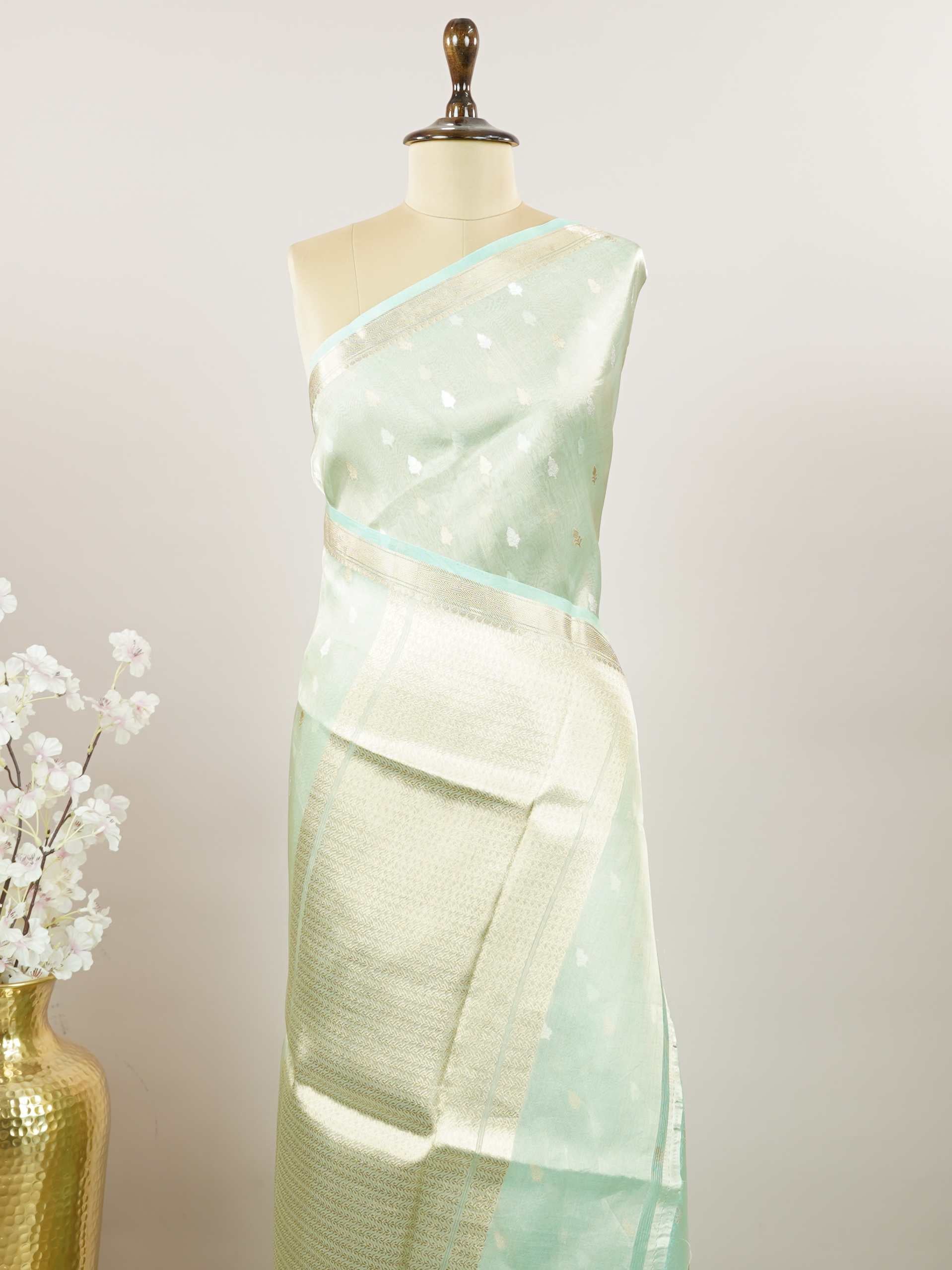 Tissue Step into subtle elegance with this tissue saree in a soothing powder green shade, paired with a matching blouse. The lightweight tissue fabric offers a soft, graceful shimmer that enhances its refined appeal. Delicate gold and silver buttas are woven throughout, adding a hint of festive charm and sophistication. Perfect for festive occasions, receptions, and elegant gatherings that call for understated beauty. Charukesi - Banarasi Tissue Kora Saree | Lightweight | Woven Buttas - Manoranjitham Weaves