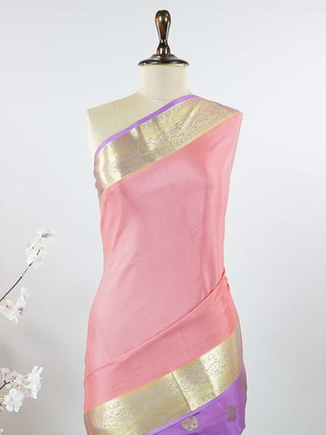 Mysore silk Gowrimanohari is a pure Mysore silk saree in the most beautiful soft rose pink — the kind of colour that feels both festive and effortlessly graceful. What makes this saree truly special is the rich purple border adorned with broad golden zari stripes that catch the light with every movement, creating a stunning contrast against the delicate pink body. The pallu carries intricate golden zari motifs woven with wonderful precision, making it a saree that looks as magnificent draped over the should