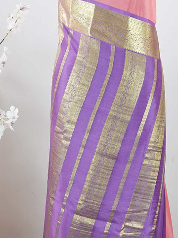 Mysore silk Gowrimanohari is a pure Mysore silk saree in the most beautiful soft rose pink — the kind of colour that feels both festive and effortlessly graceful. What makes this saree truly special is the rich purple border adorned with broad golden zari stripes that catch the light with every movement, creating a stunning contrast against the delicate pink body. The pallu carries intricate golden zari motifs woven with wonderful precision, making it a saree that looks as magnificent draped over the should
