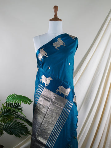 Katan A masterpiece from Varanasi, this Banarasi Katan saree in Dark Teal is a tribute to India's rich handloom legacy. The Tested Zari weaving and Motifs motifs make it a perfect choice for brides and celebrations. Every thread speaks of elegance, tradition, and the skilled hands that bring this saree to life. Sohinia - Banarasi Katan Silk Saree | Woven Motifs - Manoranjitham Weaves - Handloom Store